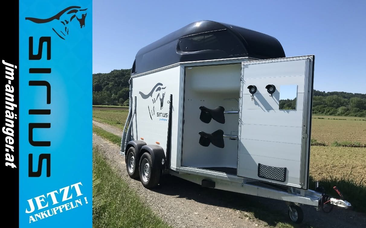 SIRIUS Pferdeanhänger auf dem Feldweg, daneben die SIRIUS-Fahne